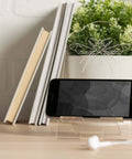Clear acrylic phone stand on a wooden desk with a curved panel featuring geometric insect design and a plant nearby