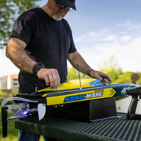 Man preparing Sonicwake RC Boat 48 Inch Self Righting Brushless 8S Ready To Run with Spektrum Smart Electronics on table.