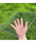 Transparent glass sheet held in hand over grass in the image.