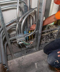 Person working on metal pipe connections in a building wall, surrounded by electrical cables and metal studs.