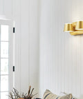 Gold three-light bathroom fixture on white wall above a door, showcasing its modern design with cylindrical shades.
