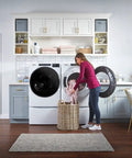 Woman loading laundry in modern laundry room with front load washer and dryer, wicker basket, bright decor