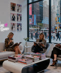 Three people reading in a modern lounge with a "Slay Queen" neon sign on the wall, city street view through the window.