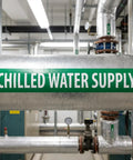 25 Pack Chilled Water Pipe Markers Vinyl Label Decals White On Green 14 Inch Long By 2 Inch High 1 1/4 Inch Letter Size Bulk For Factories And Labs Durable Weather Resistant Vinyl For Easy Identification Across Large Facilities. Green chilled water supply pipe marker on insulated pipe in facility