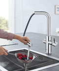 Clean Lines Single Handle Pull Out Kitchen Faucet With Laminar Spray Led Knobs For Chilled Sparkling Water Butter Smooth Pour 180 Swivel Spout in use, pouring water over berries.