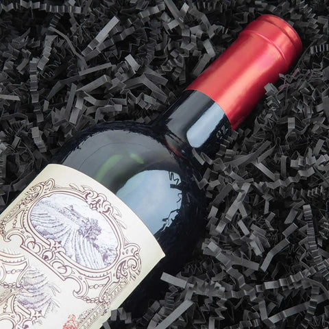 Hassle Free Black Crinkle Cut Paper Shred Filler For Gift Baskets And Boxes Smooth Cushion Wrapper surrounding a wine bottle.