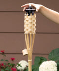 Person holding 57 Inch Bamboo Tiki Torch from Set For Outdoor Patios And Backyards, Natural Woven Torch With Fiberglass Wick And Metal Fuel Canister