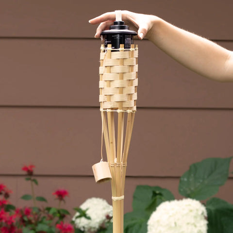 Person holding 57 Inch Bamboo Tiki Torch from Set For Outdoor Patios And Backyards, Natural Woven Torch With Fiberglass Wick And Metal Fuel Canister