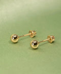 Real 14K Gold Ball Screw Back Stud Earrings For Women And Men 4mm Solid Yellow Gold Hypoallergenic And Hand Polished For Everyday Comfort And All Day Wear, pair on green background