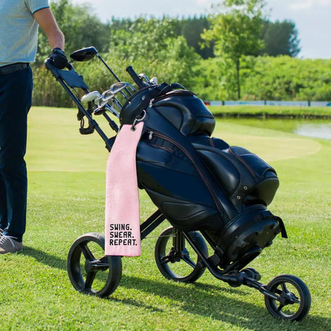 Swing Swear Repeat Embroidered Pink Golf Towel With Clip For Golf Bags on cart outdoors