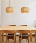 Two hand-woven rattan pendant lights above a wooden dining table, featuring 12 inch wicker shades for farmhouse vibes.