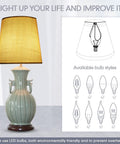 A table lamp with a beige linen shade, ceramic base, and various bulb style illustrations, showing cozy warm light glow.