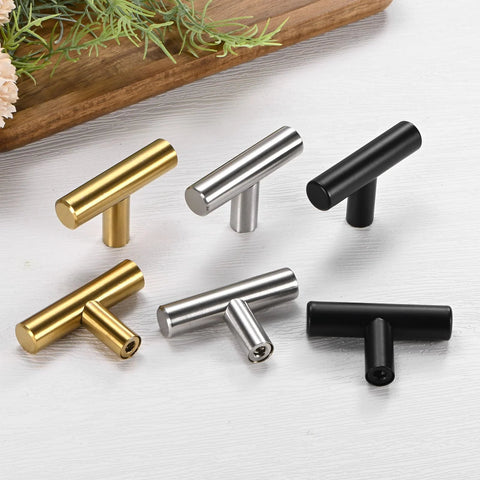Assortment of T-Bar cabinet knobs in silver, black, and gold on a surface, showcasing diverse finishes.