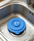 Drain Unclogger Flexible Bath Drain Cover Sealing Stopper in blue silicone placed in kitchen sink to seal drain.