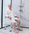 Man sitting on a Bariatric Shower Chair Heavy Duty Foldable Bath Bench With Extra Wide Seat And Private Washing Cutout 350 Lb Weight Capacity Non Slip Legs Ideal For Seniors Elderly Disabled And Pregnancy Bathing in a modern shower.