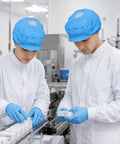 Two workers in white lab coats wearing Five Pack Blue Anti Static Caps Featuring Breathable Mesh Panels and Reliable Dust Blocking Defense for Cleanrooms.