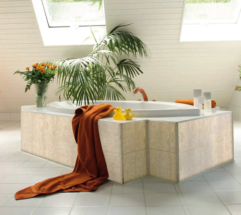 Modern bathroom with white corner bathtub, green plant, orange towel, and rubber ducks on tiled floor under skylight windows.
