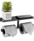 Double Roll Toilet Paper Holder With Shelf Matte Black Brass Finish, holding two rolls, small plant, and phone on the upper shelf