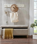 Beige upholstered bench with soft cushion, decorative pillow, and wood legs on hardwood floor in cozy living room corner.