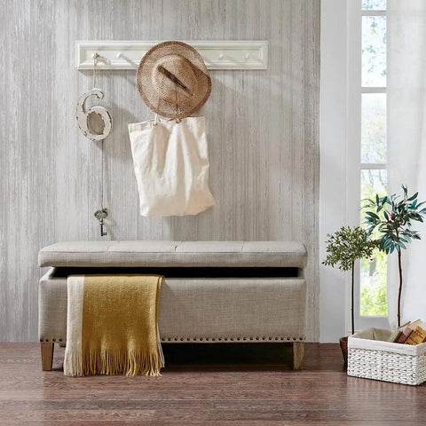 Beige upholstered bench with soft cushion, decorative pillow, and wood legs on hardwood floor in cozy living room corner.