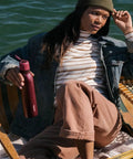 Person relaxing on a boat holding FreeSip Twist Insulated Stainless Steel Water Bottle With Straw For Sports and Travel, 24 oz Black Cherry.