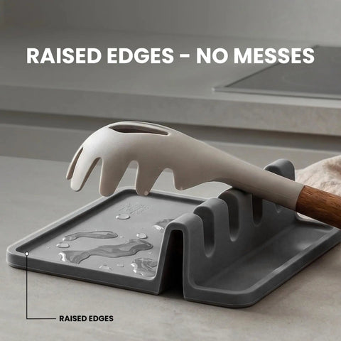 Gray high heat silicone spoon rest drip pad with raised edges, four slots holding utensils, BPA free, on kitchen counter.