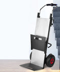 Super Slick Electric Stair Climber Cart That Folds Like A Champ With Massive Battery Life To Haul Heavy Cement Or Sand Up Stairs Without Breaking A Sweat At 550 Pounds Capacity Plus Smooth Motorized Grip For Any Tough Job, showing the cart near stairs.