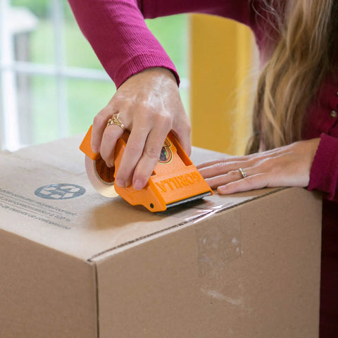 Person using Tough And Wide Packing Tape With Dispenser For Moving And Shipping, Crystal Clear 2.83 Inch By 20 Yard on box