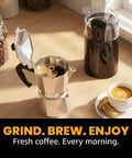 Elite Gourmet ECG914 Electric Coffee And Spice Grinder Heavy Duty Stainless Steel Blade One Touch Operation Black Compact Design with coffee pot and cup.