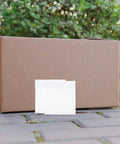 Fifty Pack Small Bubble Mailers 10x10 Plus 3cm Self Seal Padded Envelopes next to a large shipping box outdoors.