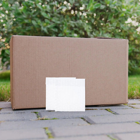 Fifty Pack Small Bubble Mailers 10x10 Plus 3cm Self Seal Padded Envelopes next to a large shipping box outdoors.