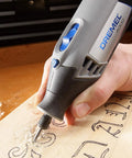 Person using All-Purpose Rotary Tool Accessory Kit With 110 Pieces Including Carving Bit Sanding Drums Grinding Stones Cutting Discs And A Storage Case Gray Ideal For DIY Projects And Home Improvement Tasks to carve wood, close-up.