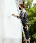 Person using Badass Paint Pressure Pot With 2 Liter Tank And Dual Spray Guns Plus Long Hoses for painting wall from ladder.