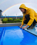 Heavy Duty Roofing Underlayment Tape being applied by a person in a yellow raincoat on a roof with a rainbow in the background.