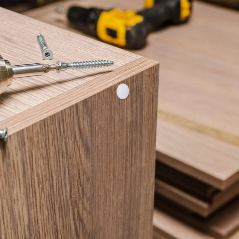 Four Sizes White Plastic Hole Plugs For Cabinet And Furniture installed on wooden surface, covering screw hole next to drill.