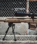 Man aiming Barrett Licensed M98B MRAD AEG Airsoft Rifle with folding stock in tan finish at shooting range