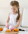 Child wearing Kids Cut Resistant Gloves Level 5 Four Pairs Pack In Bright Colors For Kitchen Prep, slicing fruit with a knife.