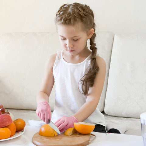 Child wearing Kids Cut Resistant Gloves Level 5 Four Pairs Pack In Bright Colors For Kitchen Prep, slicing fruit with a knife.