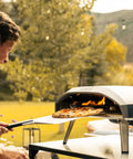 Koda 16 Inch Propane Gas Pizza Oven with 28 MBAR Regulator and Hose, outdoor setup with pizza being cooked, Foundry Black.