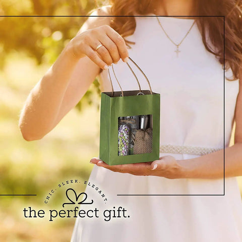 Person holding a Green Kraft Paper Gift Bag with handles and clear window, medium size, showing contents for kids' party gifts.