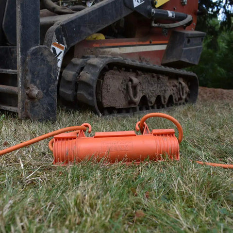Bright orange Heavy Duty Outdoor Extension Cord Safety Cover on grass near construction equipment, protecting cord connections.
