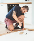 Man using drill to install brass table hinges 2-piece set for Butler tray and cabinet furniture on wooden floor