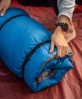 Person securing blue sleeping bag with 'Two Pack 48 Inch Sleeping Bag Straps With Quick Release Buckles For Universal Fit' in red tent.