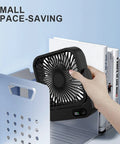 Magnetic Travel Fan With Five Adjustable Speeds Cruise Ship Approved Battery Powered Personal Cooler in black being held near books.