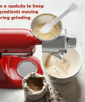 Red KitchenAid stand mixer with all-metal grain mill attachment on top, grinding oats into flour.