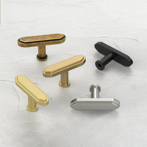 Assorted cabinet handles including brushed antique, brass, black, and silver finishes on a white textured surface.
