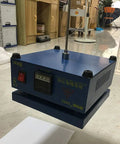 Blue electronic device on floor, focus unclear, possibly workshop setting, various office items in background.