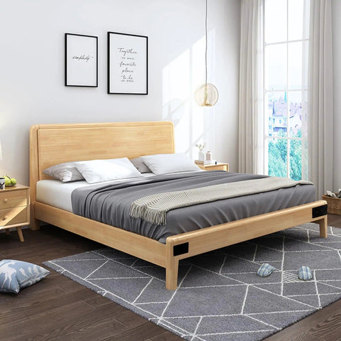 Modern bedroom with wooden bed frame, gray bedding, and decorative pillows in a well-lit room with large windows and wall art.