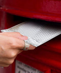 Hand inserting 50 Pack 7x9 Inch Metallic Bubble Mailers Silver Self Seal Padded Envelopes into red mailbox for shipping protection