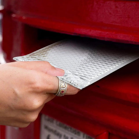 Hand inserting 50 Pack 7x9 Inch Metallic Bubble Mailers Silver Self Seal Padded Envelopes into red mailbox for shipping protection